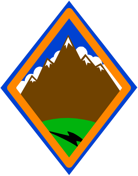 The image shows a stylized camping emblem with an outdoor scene featuring mountains under blue sky on top of what appears to be a brown triangle inside another larger orange-brown diamond shape against a dark background, suggesting it could represent a logo for a campsite or outdoors activity area.