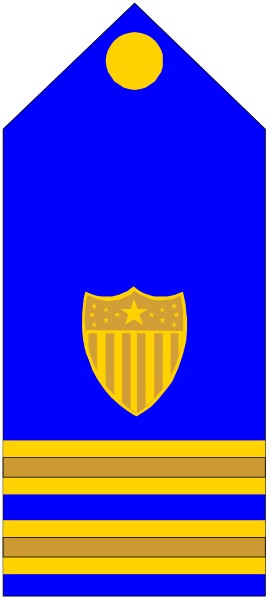 The image shows a blue flag with an emblem of a shield on it, placed next to what appears to be a yellow ribbon in front of two stripes that alternate between red and white.