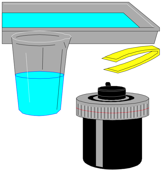 The image shows a blackboard with various items on it: an empty beaker at top left corner; two test tubes in center right side of board; blue liquid inside one tube near bottom middle part of board, and yellow substance above that same tube; small white object resembling a lid or cap next to the second test tube.