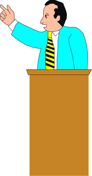 The cartoon shows a man standing at a podium with his hand raised as if speaking to an audience; he is wearing a blue suit jacket over a yellow shirt and has dark hair.