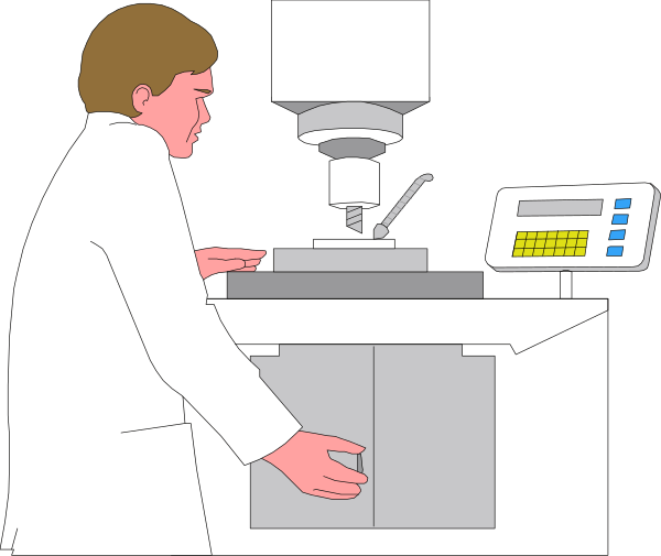 The image shows a man standing at an industrial machine with various buttons on it; he is wearing white lab attire including goggles hanging around his neck.