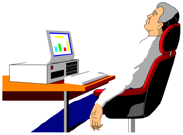 The image shows a man sitting at an office desk with his feet up on another chair; he is looking down towards some papers in front of him while using a computer monitor that displays graphs.