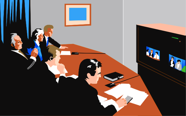 The image shows a group of five individuals seated around an oval table with papers on it; there is a television screen displaying three faces in front of them against a blue background.