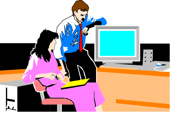The image shows a man standing next to an office desk with two computer monitors on it; he is gesturing towards something off-screen while another person sits at the desk using one of the computers.