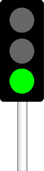 The image shows a traffic light with two green lights on it against an urban background that includes buildings and roads.