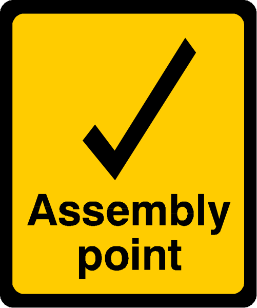 The image shows a yellow sign with black text that reads "Assembly Point" next to an icon of a checkmark inside a circle.