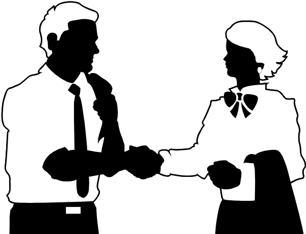 The black and white photo shows two men standing next to each other with a blurred background that suggests an indoor environment; both individuals appear engaged in conversation as one man is gesturing towards something off-camera while holding what seems like papers, possibly discussing business matters or sharing information.