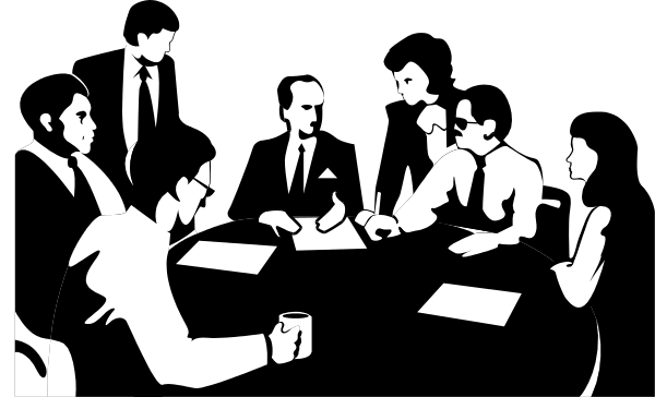 The black and white photo shows a group of business professionals sitting around a conference table with papers on it; some individuals appear to be engaged in conversation while others look at documents.