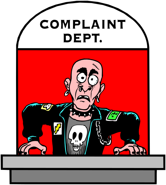 The cartoon shows a man with an exaggeratedly large head sitting behind a counter labeled "COMPLAINT DEPT." He is wearing sunglasses on his forehead and has tattoos visible above them; he's also holding up two fingers in front of him, as if making the peace sign.