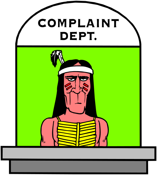 The image shows a cartoon of an indigenous man with feathers on his head standing behind a sign that reads "COMPLAINT DEPT."